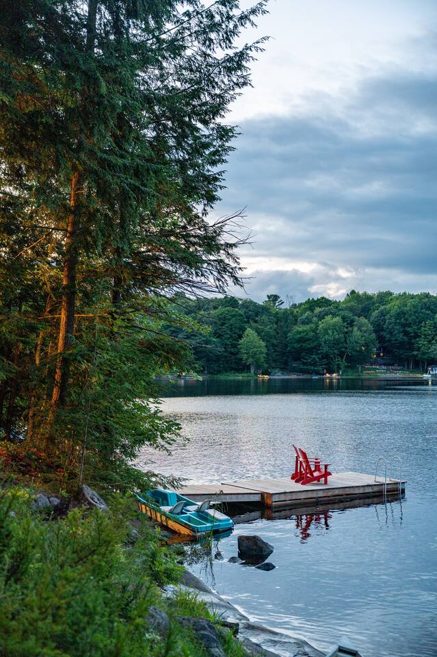 Private dock with red Muskoka chairs and kayaks on calm lake